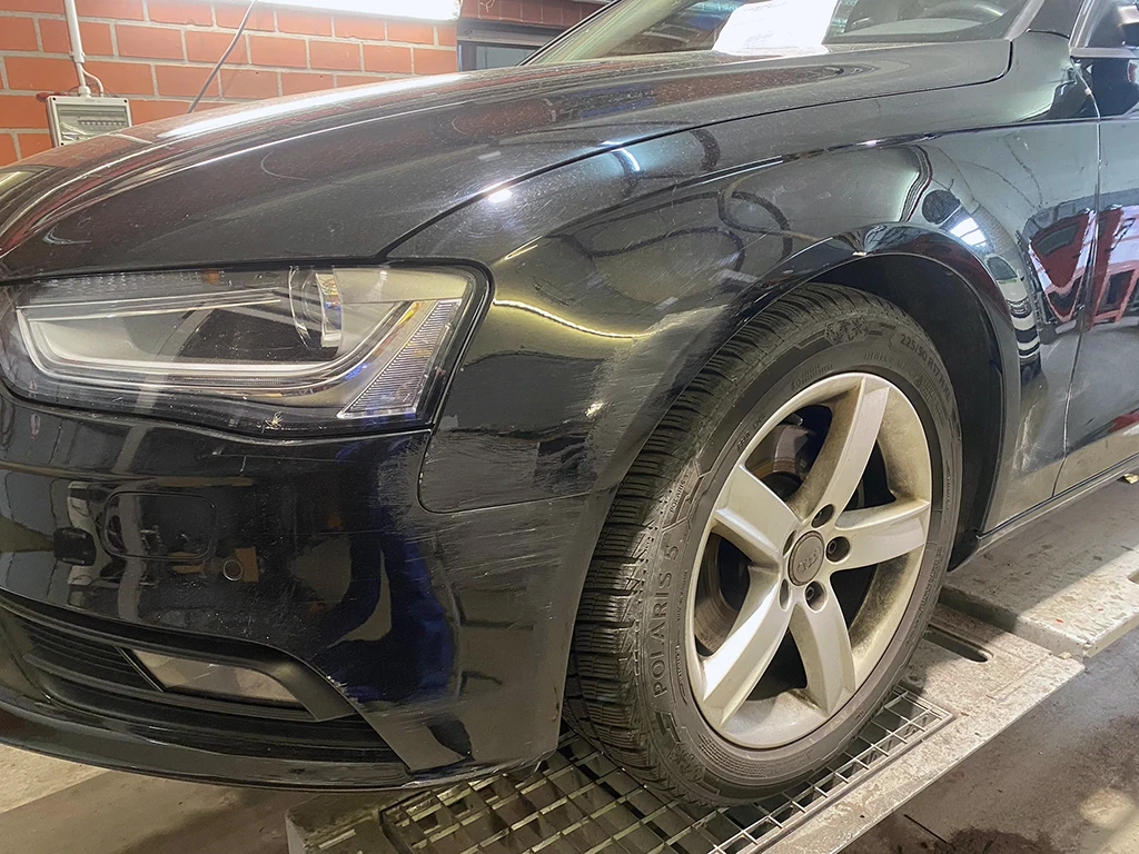 Audi mit beschädigter Fahrzeugseite vor der Unfallschaden-Reparatur in der Werkstatt.