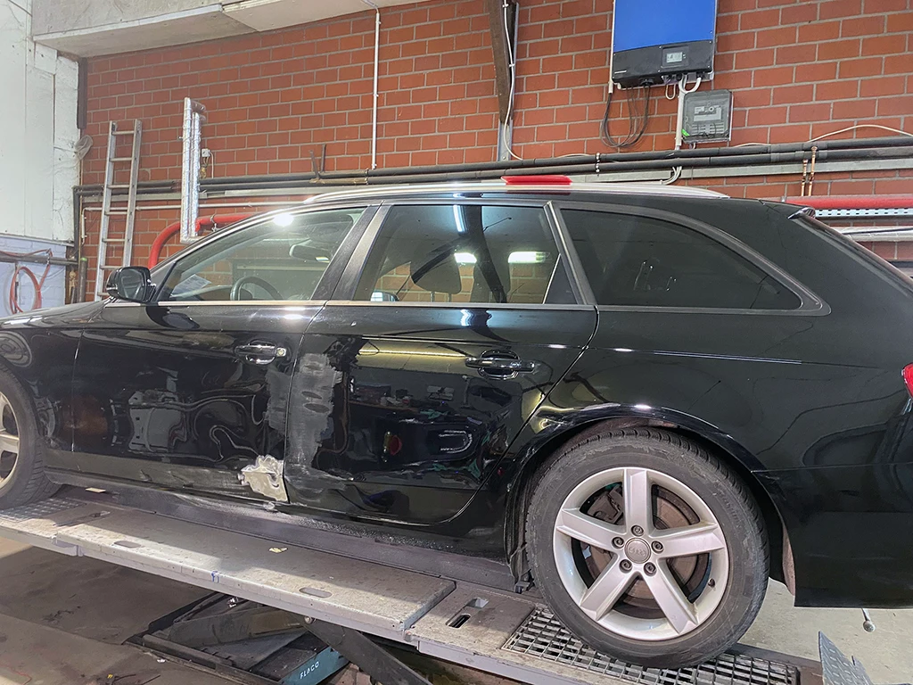 Seitenansicht eines schwarzen Audi mit Seitenschaden vor den Karosseriearbeiten.